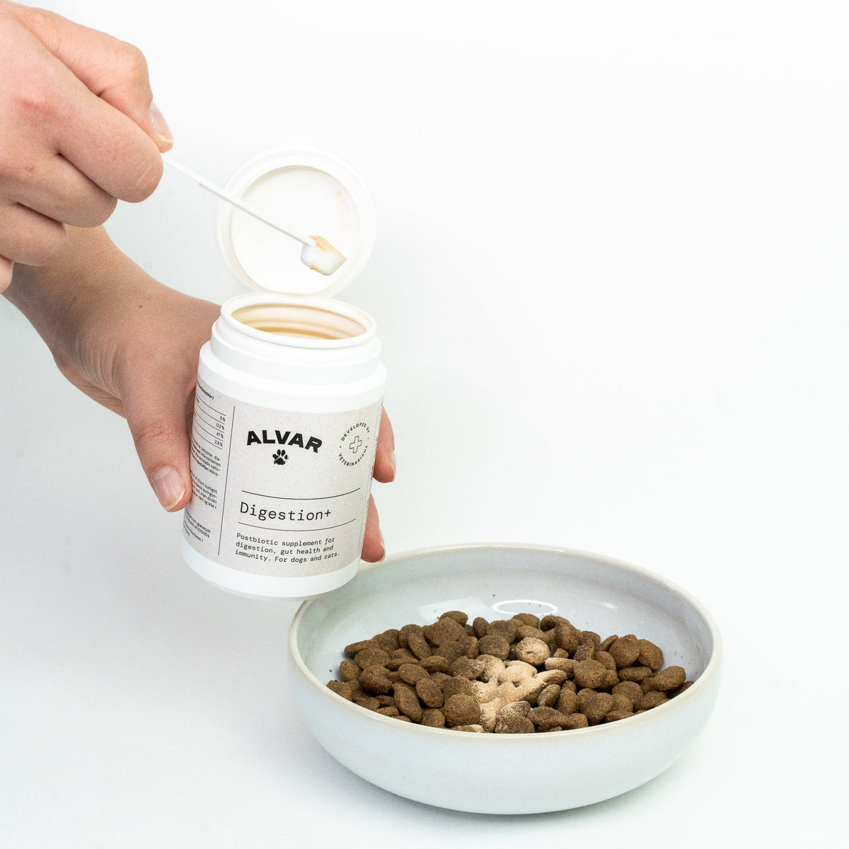 Person holding an Alvar Pet Digestion+ supplement jar with pet food in a bowl on a white background