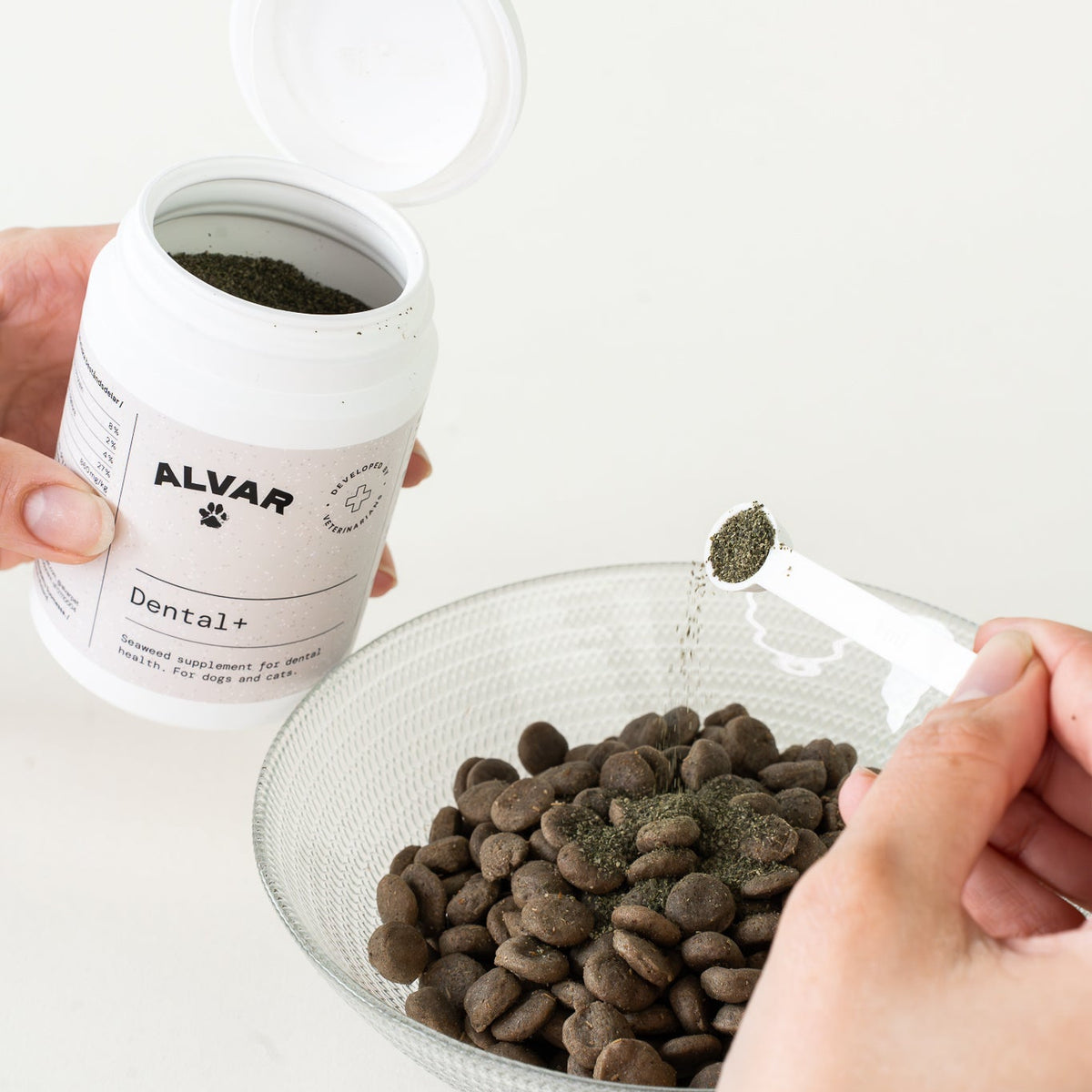 Person adding Alvar Dental+ pet food supplement to a bowl of food.